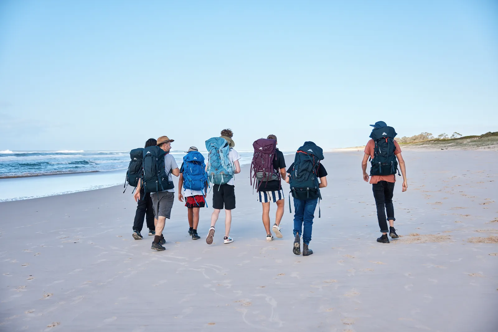 A small group walking together along the beach at dawn carrying packs