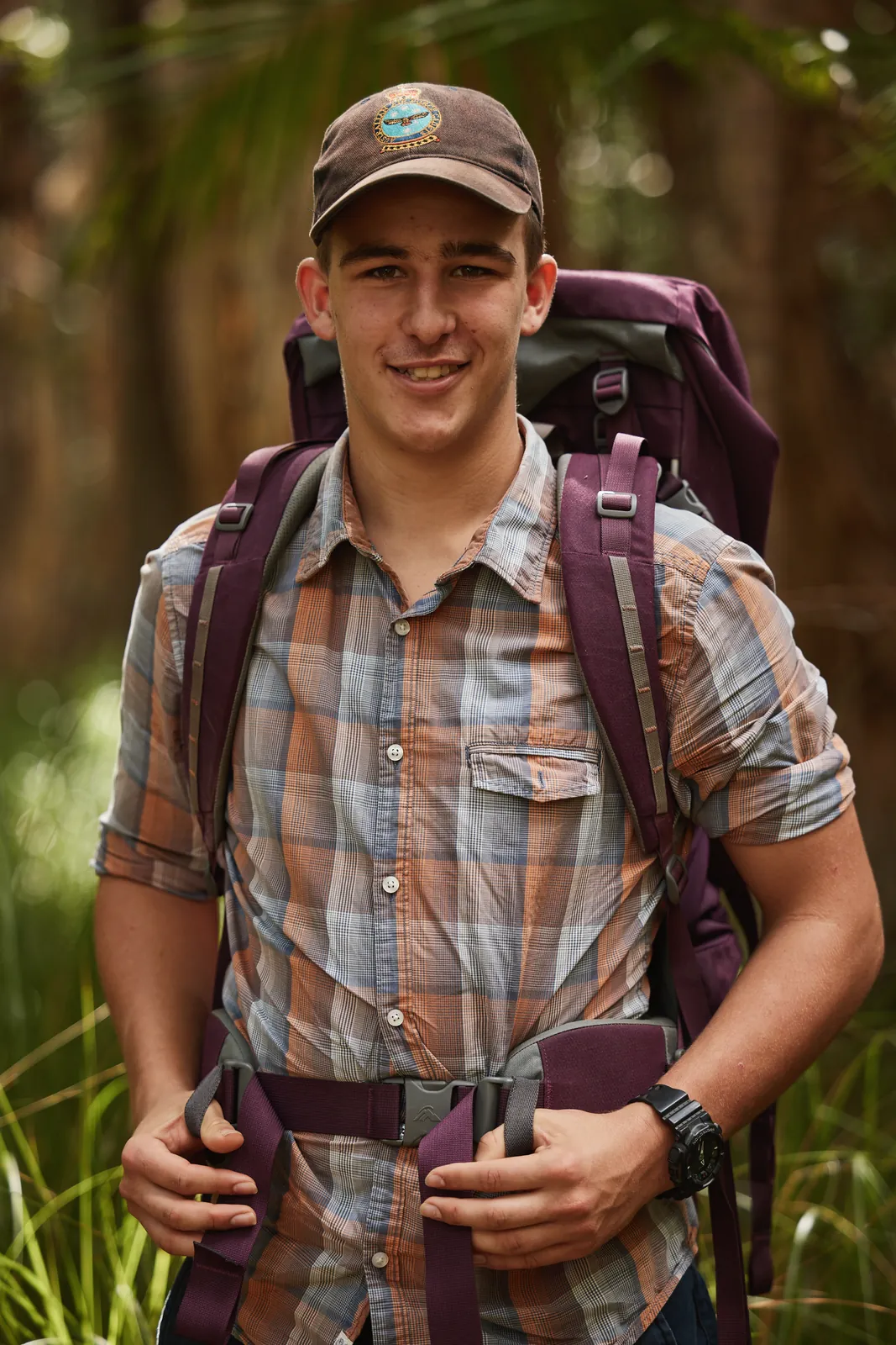 A young man standing in bushland wearing a hiking pack